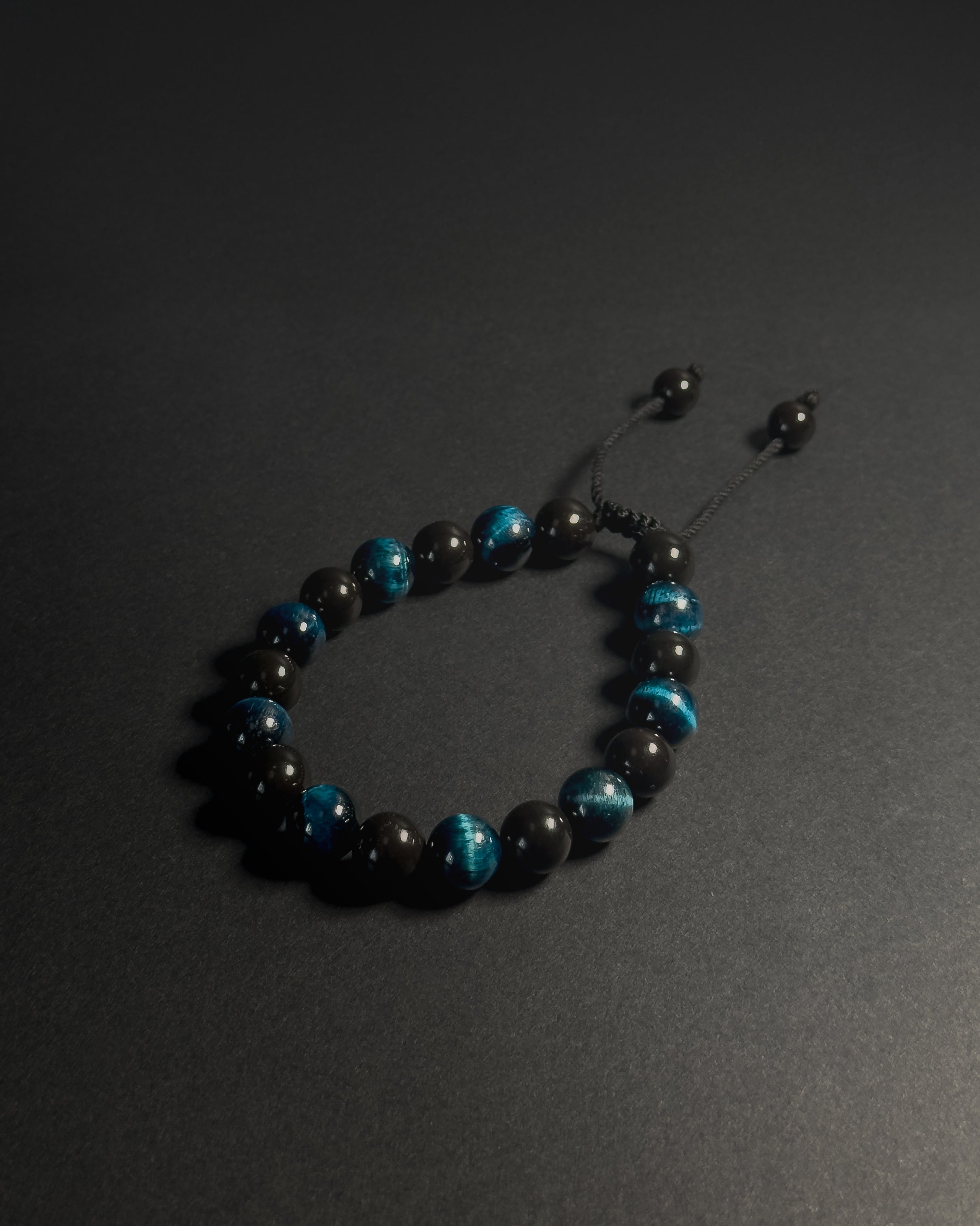 Black and blue beaded bracelet on a dark surface. Black beaded bracelet with blue tiger eye 