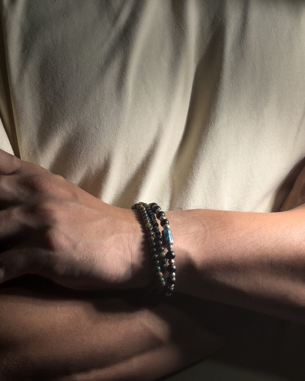 A close-up of a person's wrist wearing stacked bracelets, with a cream-colored shirt in the background.