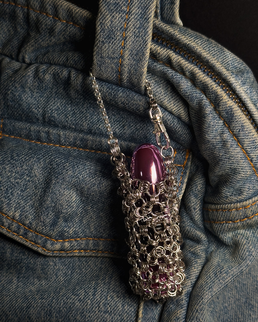 A stainless steel chainmail sleeve holding a glossy purple capsule mac lipstick, draped over a blue denim purse.