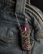 A stainless steel chainmail sleeve holding a glossy purple capsule mac lipstick, draped over a blue denim purse.
