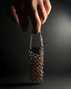 A hand holding a small stainless steel chainmail sleeve filled with lighter against a dark, spotlighted background.