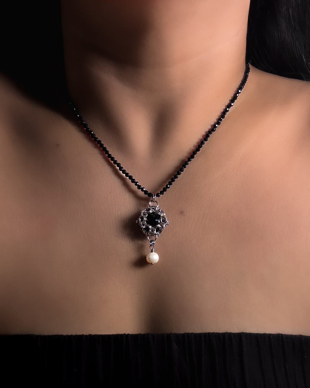 A close-up of a model's neck and chest wearing a stainless steel chainmail necklace with 14mm black onyx pendant, freshwater pearl and faceted spinel beads.