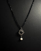 Stainless steel chainmail necklace with 14mm black onyx pendant, freshwater pearl and faceted spinel beads against a dark background.