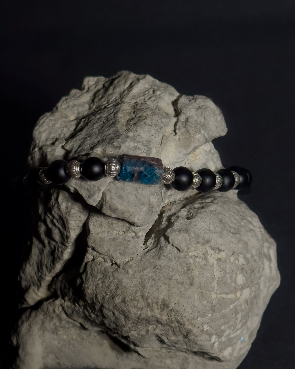 Handmade Beaded Bracelet Featuring Blue Apatite and matte Black Onyx displayed on a natural gray rock against dark background