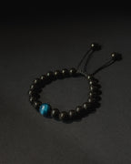 Black beaded bracelet with a blue bead on a dark background. Black beaded bracelet with blue tiger eye.