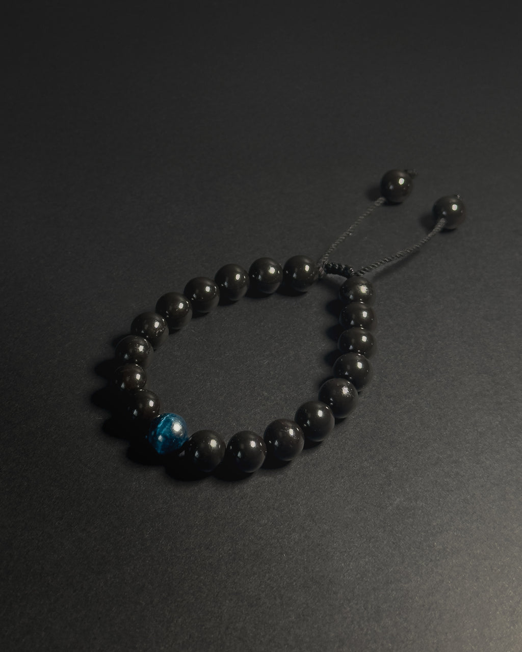 Black beaded bracelet with a blue accent bead on a dark background