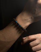 Close-up of a wrist wearing a black beaded bracelet with blue tiger eye against a dark background