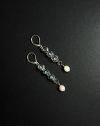 A pair of silver drop earrings featuring light blue topaz beads, silver wirework, and white pearl, displayed on a dark textured background.