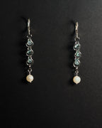 A pair of silver leverback dangle earrings featuring blue topaz capture bead and a round white pearl at the bottom, displayed on a dark background.