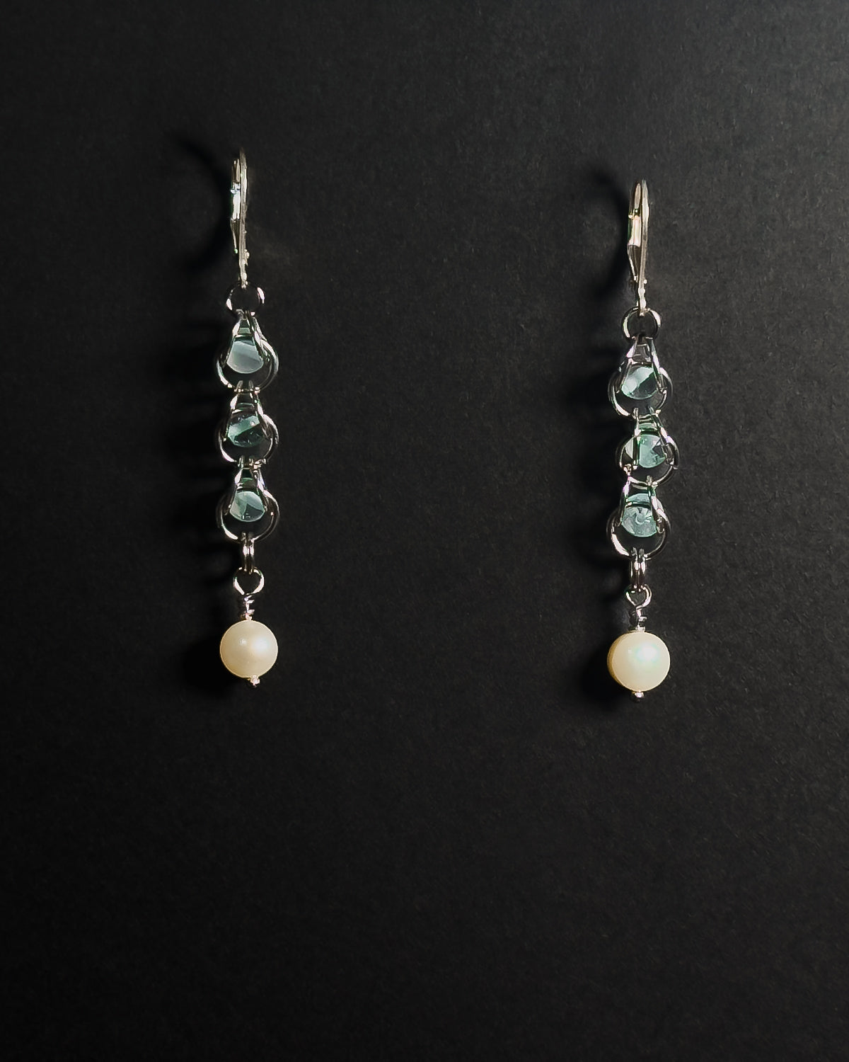 A pair of silver leverback dangle earrings featuring blue topaz capture bead and a round white pearl at the bottom, displayed on a dark background.
