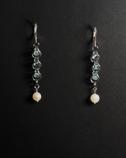 A pair of silver leverback dangle earrings featuring blue topaz capture bead and a round white pearl at the bottom, displayed on a dark background.