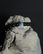 A beaded bracelet with mostly tourmaline and a sodalite bead, displayed on a gray rock against a black background.