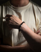 A close-up of a person wearing a black tourmaline beaded bracelet with a sodalite center stone on their wrist, wearing a beige t-shirt.