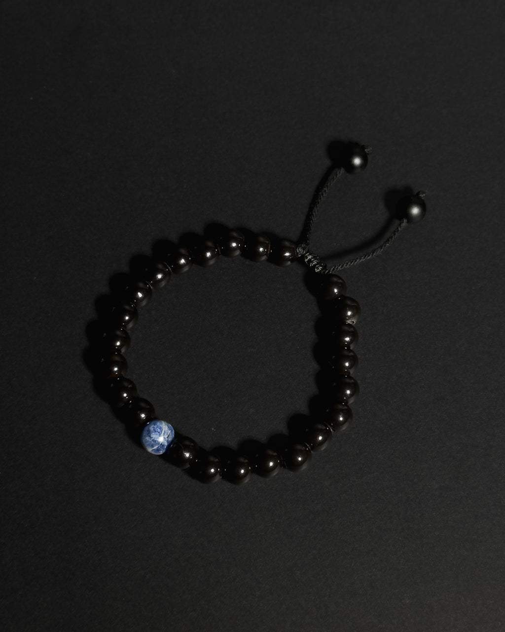 A beaded bracelet made of tourmaline with a single sodalite, shown on a dark background.
