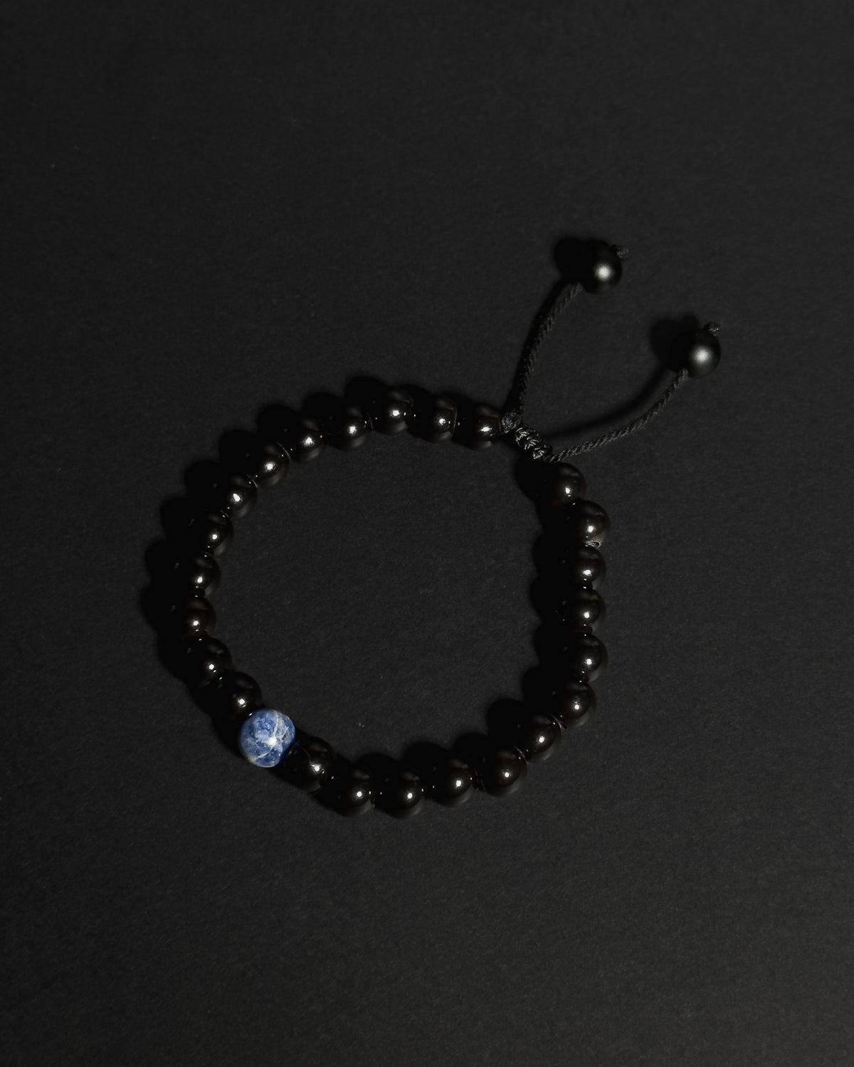 A beaded bracelet made of tourmaline with a single sodalite, shown on a dark background.