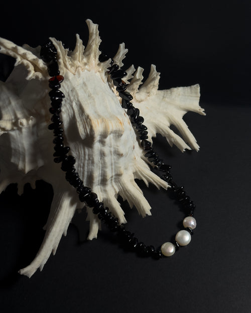 Black beaded necklace with pearls on a large shell against a dark background