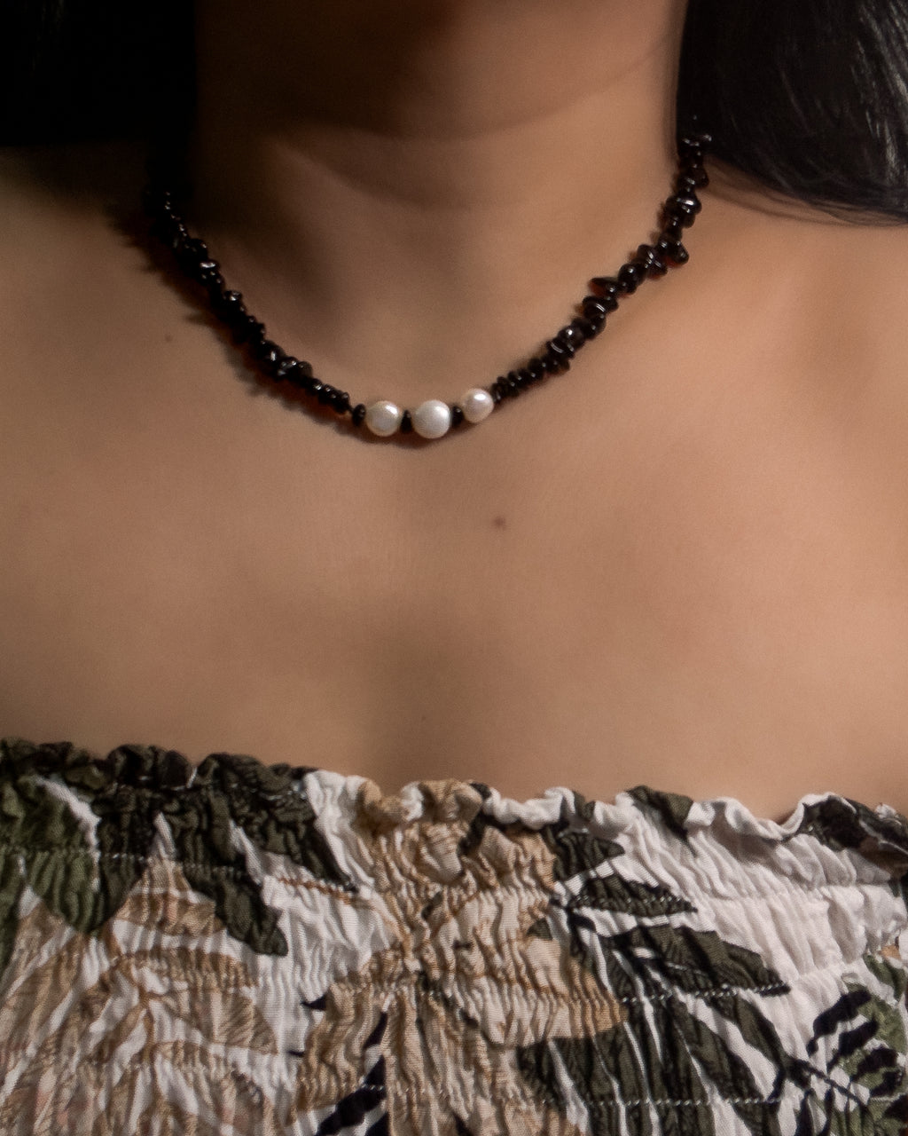 Necklace with black and white beads on a person wearing a patterned top.