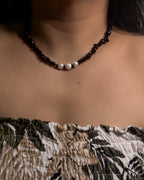Necklace with black and white beads on a person wearing a patterned top.