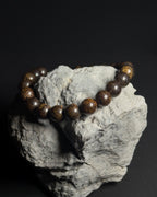 Handmade Trailborn Bracelet on a grey rock featuring 8mm natural bronzite beads with adjustable sliding knot closure on a dark background.