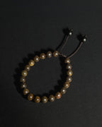 A beaded bracelet made of natural bronzite stone, featuring a dark adjustable cord closure with metal beads, displayed on a dark background.