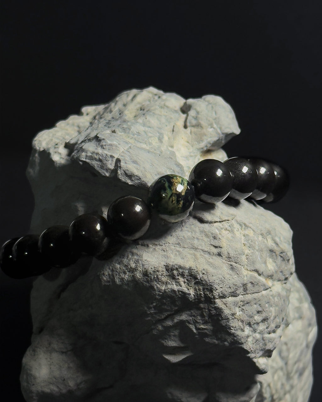 Handmade adjustable Wildstone bracelet featuring natural Kambaba jasper with black tourmaline shot on top of a natural grey rock against black background.