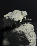 Handmade adjustable Wildstone bracelet featuring natural Kambaba jasper with black tourmaline shot on top of a natural grey rock against black background.