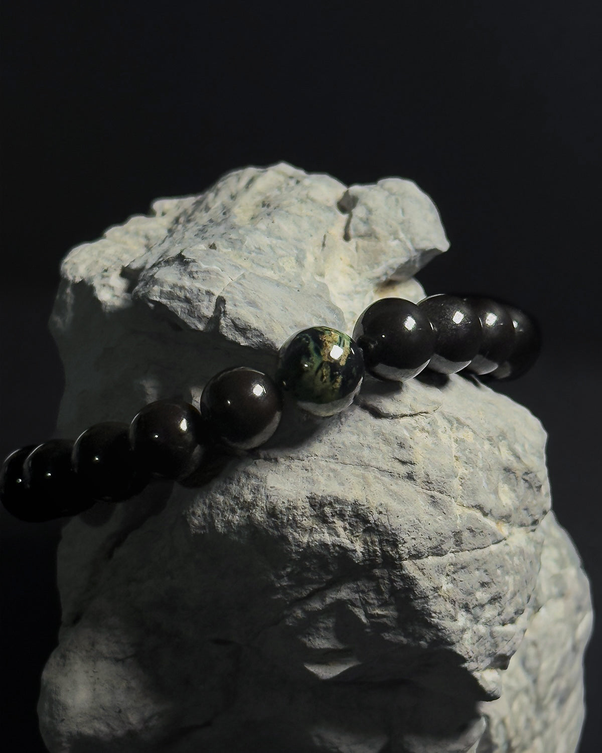 Handmade adjustable Wildstone bracelet featuring natural Kambaba jasper with black tourmaline shot on top of a natural grey rock against black background.