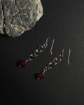 Stainless Steel hooked dangle earrings made with jumprings link by link with a geometric garnet against dark background with a natural rock.