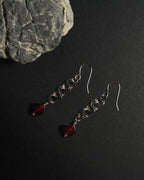 Stainless Steel hooked dangle earrings made with jumprings link by link with a geometric garnet against dark background with a natural rock.