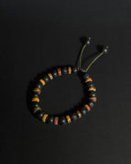 A beaded adjustable bracelet featuring black lava stones, and picasso jasper, with an adjustable green cord closure, displayed on a dark background.