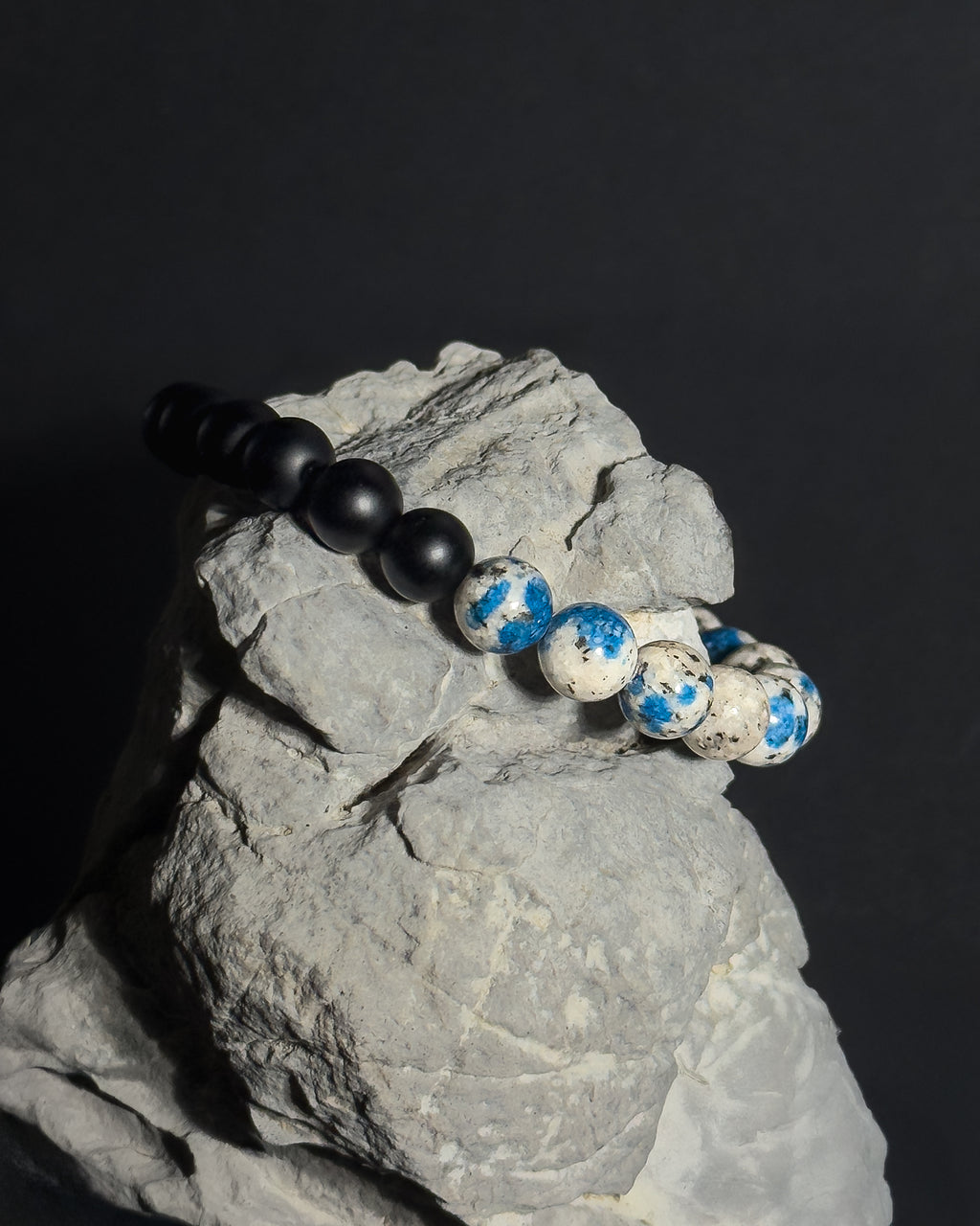 Handmade natural K2 and Matte Black Onyx adjustable bracelet draped on natural gray stone