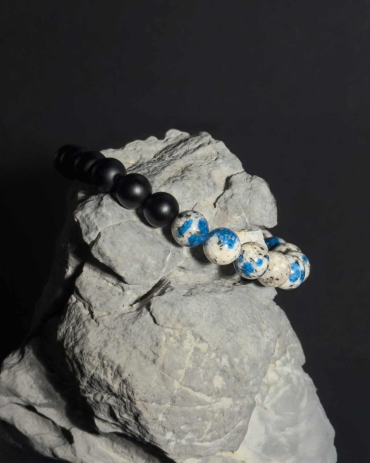 Handmade natural K2 and Matte Black Onyx adjustable bracelet draped on natural gray stone
