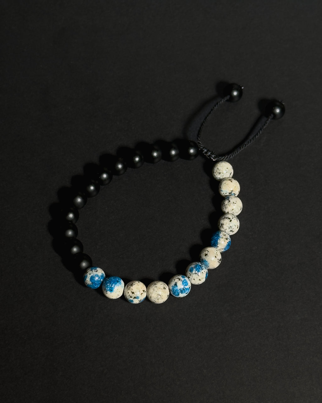 Handmade natural K2 and Matte Black Onyx adjustable bracelet aainst dark background.