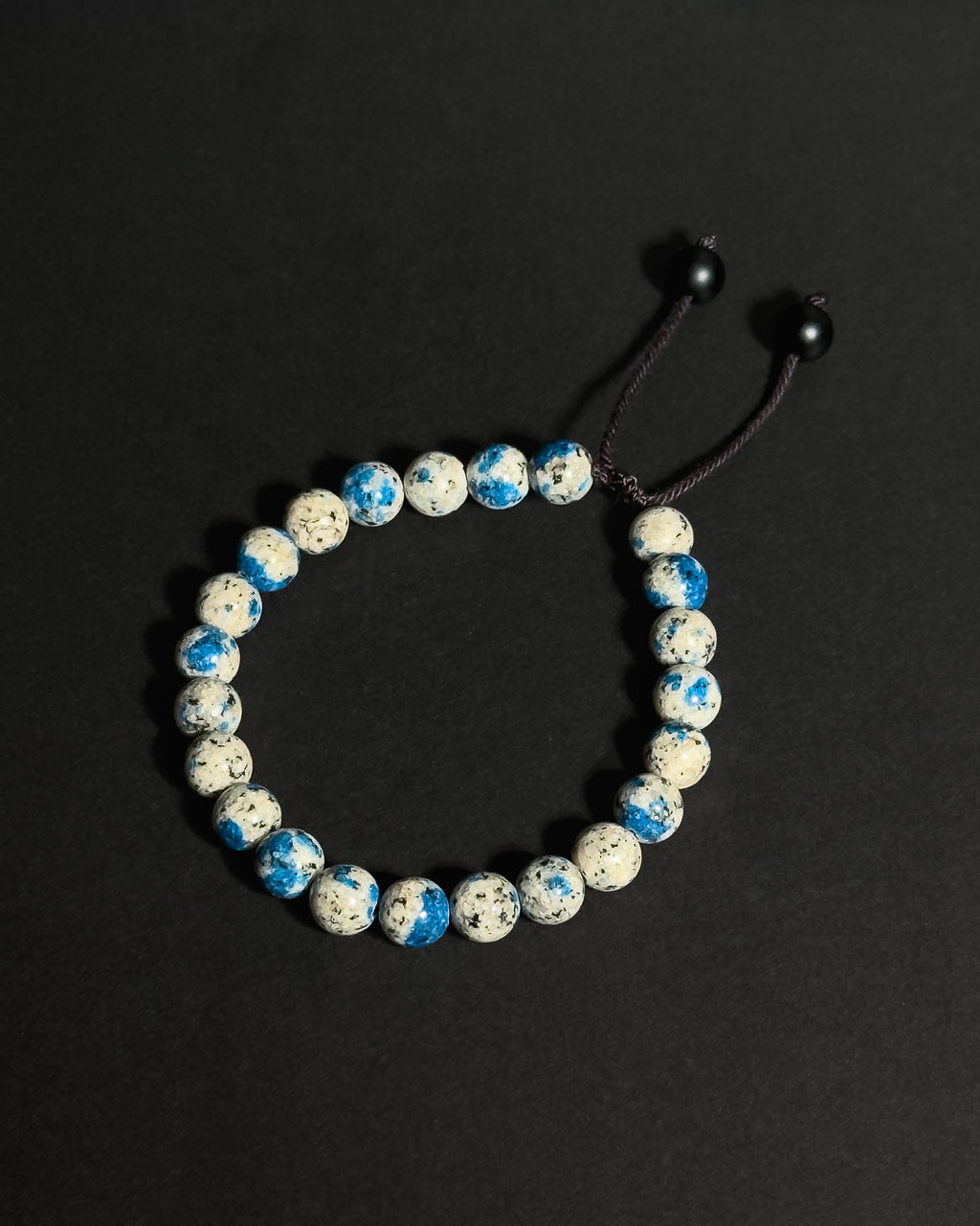 A beaded stretch bracelet made of K2 stone beads, with a dark brown adjustable cord displayed on a dark background.