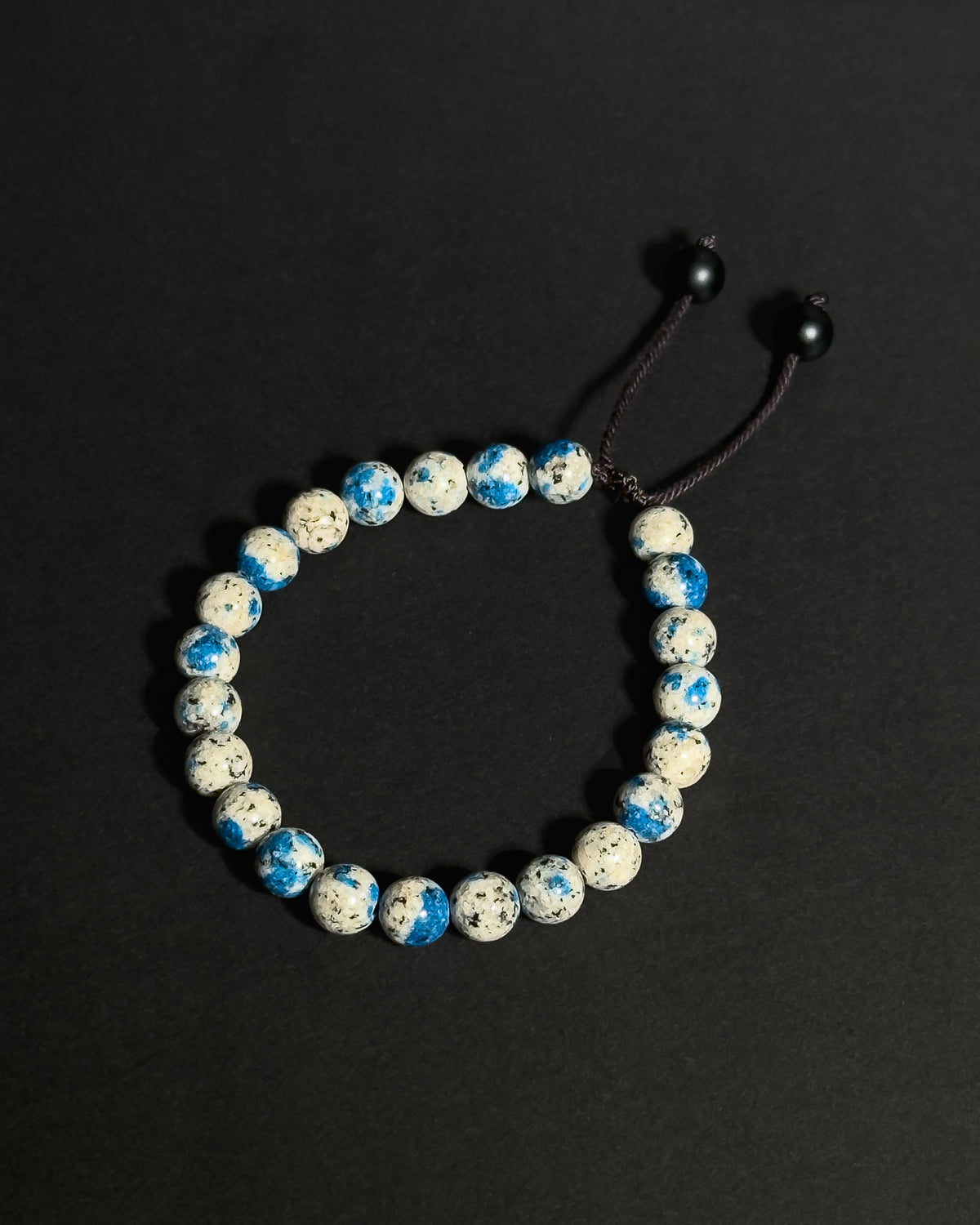 A beaded stretch bracelet made of K2 stone beads, with a dark brown adjustable cord displayed on a dark background.