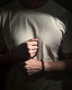 Model in cream shirtwearing a handmade adjustable Wildstone bracelet featuring natural Kambaba jasper with lava stone, and holding a handmade adjustable Wildstone bracelet featuring natural Kambaba jasper with black tourmaline.