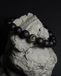Handmade adjustable Wildstone bracelet featuring natural Kambaba jasper with lava stone on top of a natural grey rock against dark background