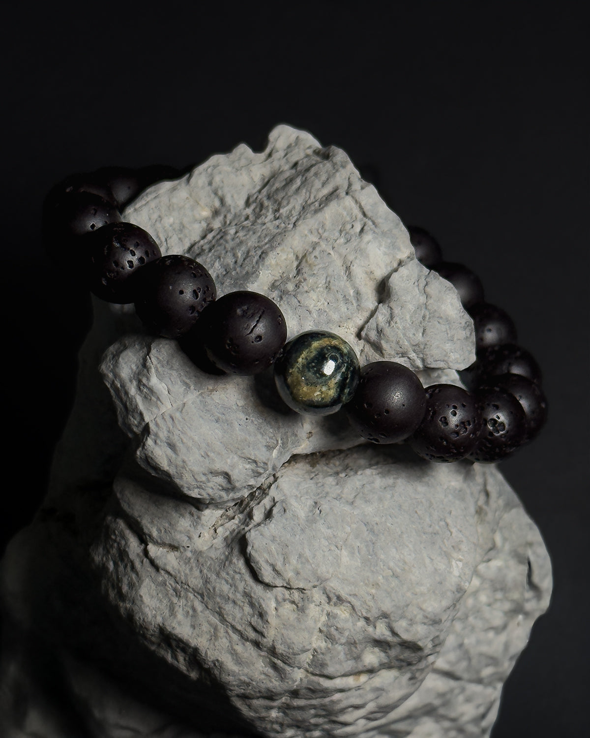 Handmade adjustable Wildstone bracelet featuring natural Kambaba jasper with lava stone on top of a natural grey rock against dark background