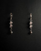 A pair of silver dangle earrings with rose quartz crystal capture bead and dark gray pearl drops, displayed on a black background .