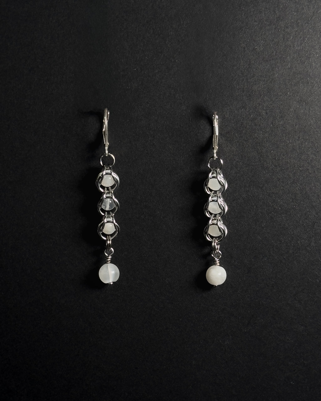 A pair of silver drop earrings with white round beads, displayed on a black background 