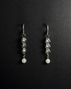 A pair of silver drop earrings with white round beads, displayed on a black background 