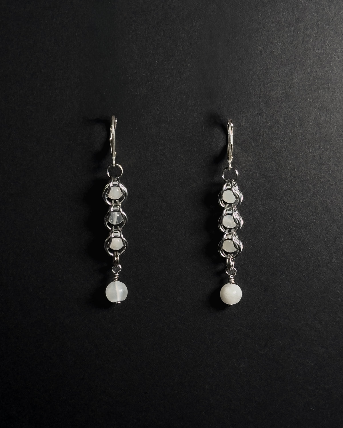 A pair of silver drop earrings with white round beads, displayed on a black background 