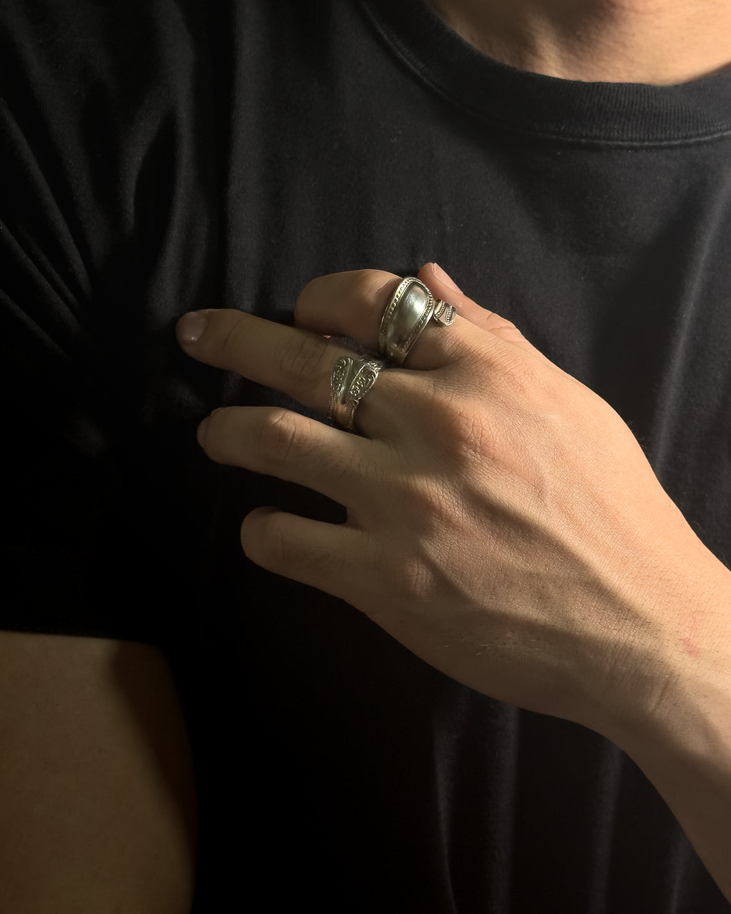A close-up of a person's hand wearing two Solid stainless steel spoon ring  rings, including one wide band ring and one textured ring, against a black t-shirt.