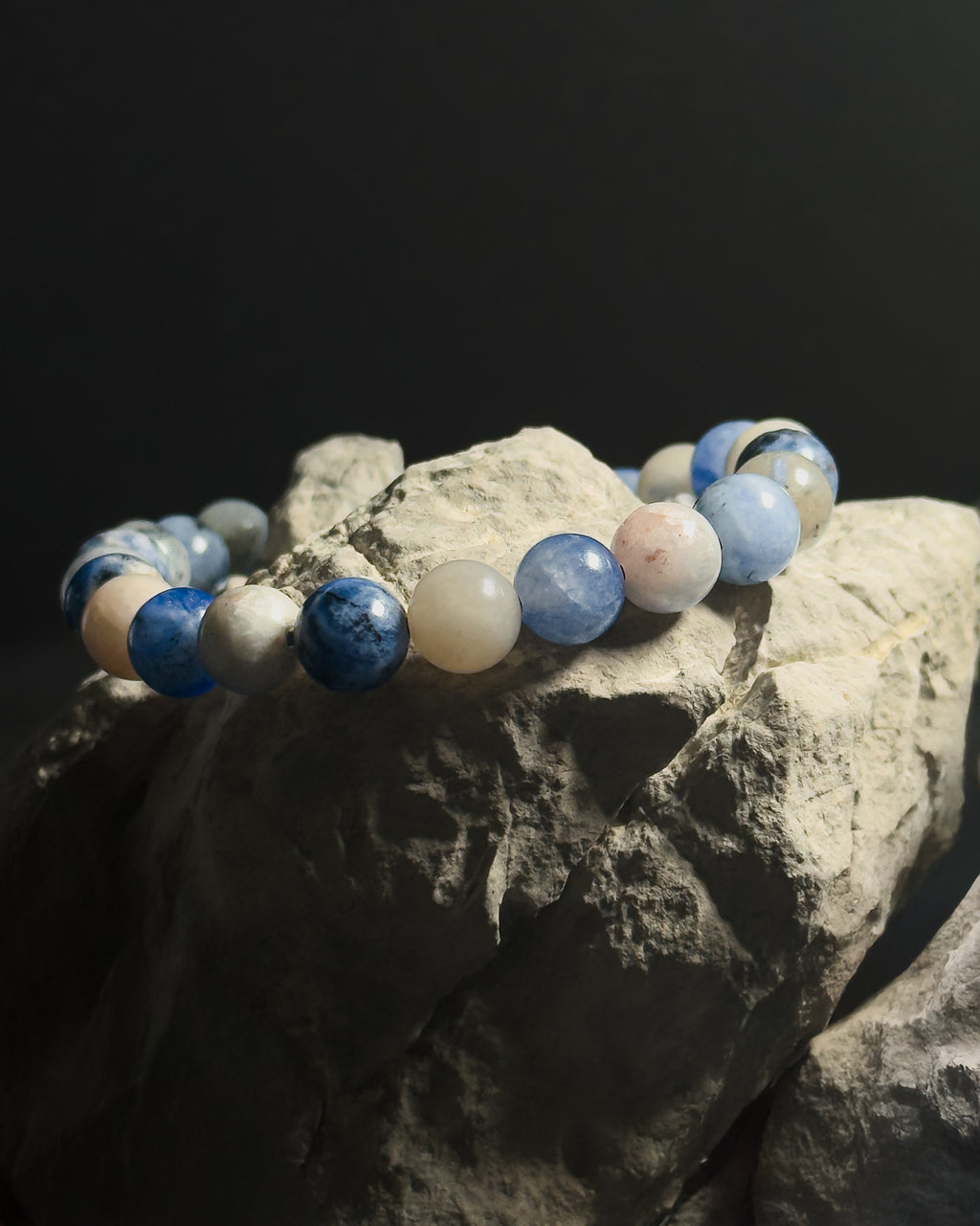 A beaded bracelet made of polished sodalite stone displayed on a textured gray rock against a dark background.