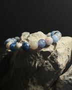 A beaded bracelet made of polished sodalite stone displayed on a textured gray rock against a dark background.