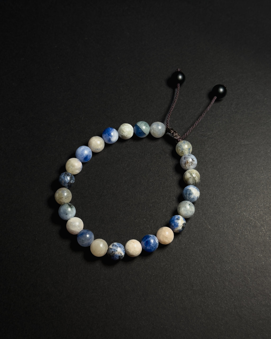 A beaded stretch bracelet made of sodalite, with a dark brown cord and black sliding beads, displayed on a dark gray background.