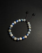 A beaded stretch bracelet made of sodalite, with a dark brown cord and black sliding beads, displayed on a dark gray background.