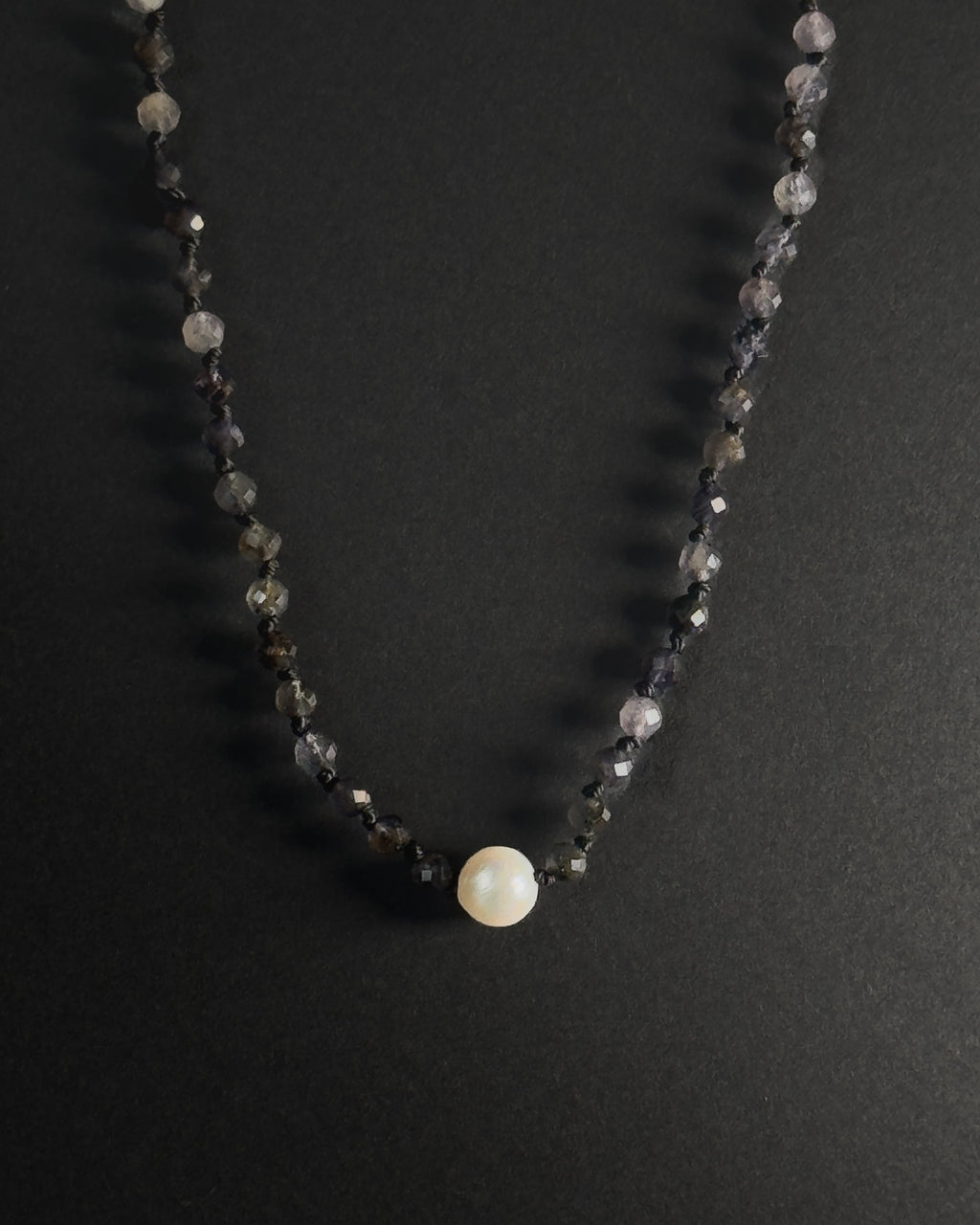 Necklace with black beads and a central pearl on a dark background