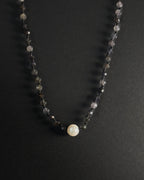 Necklace with black beads and a central pearl on a dark background