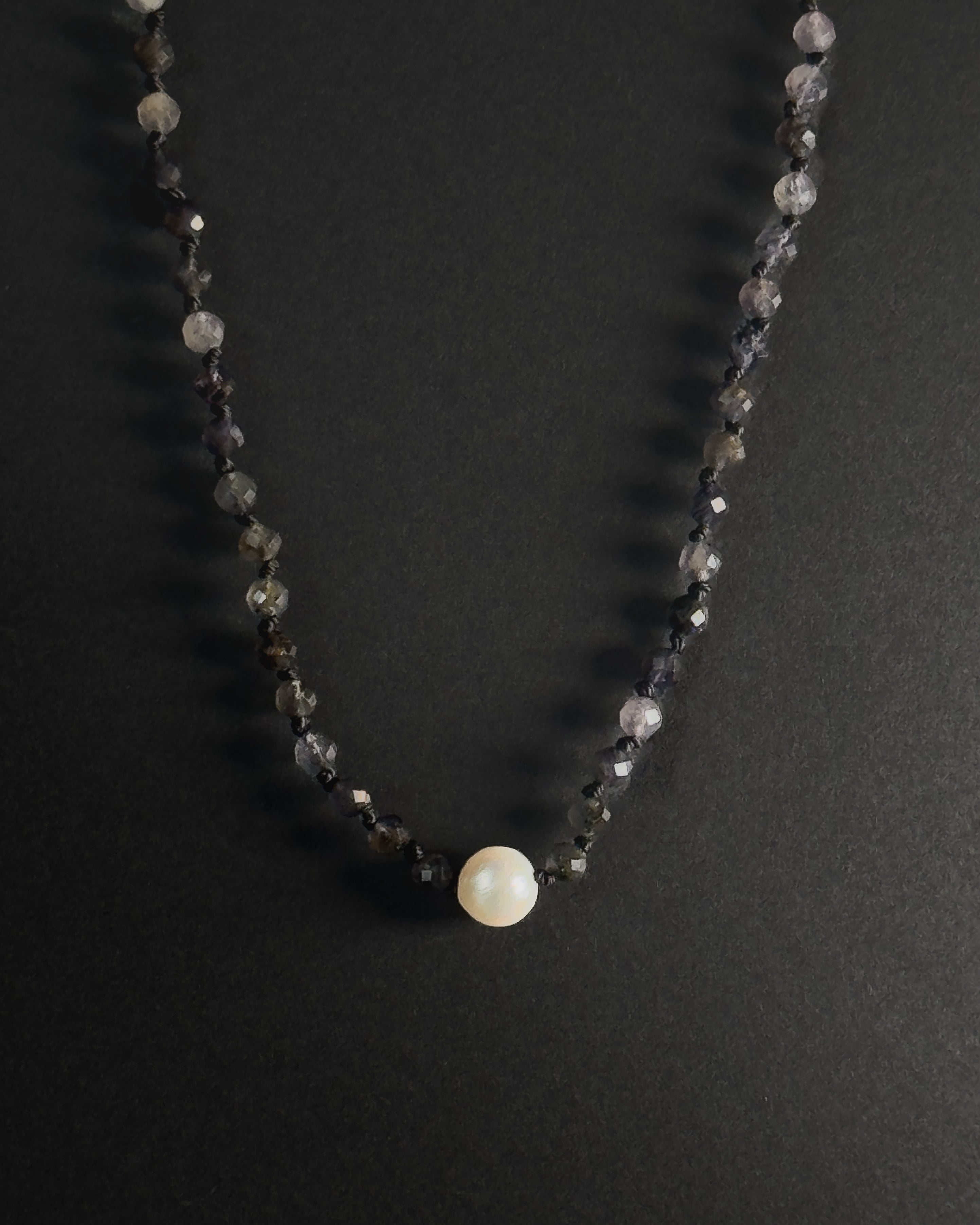 Necklace with black beads and a central pearl on a dark background